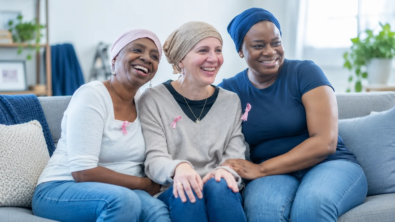 Three smiling women in head coverings sitting together on a sofa